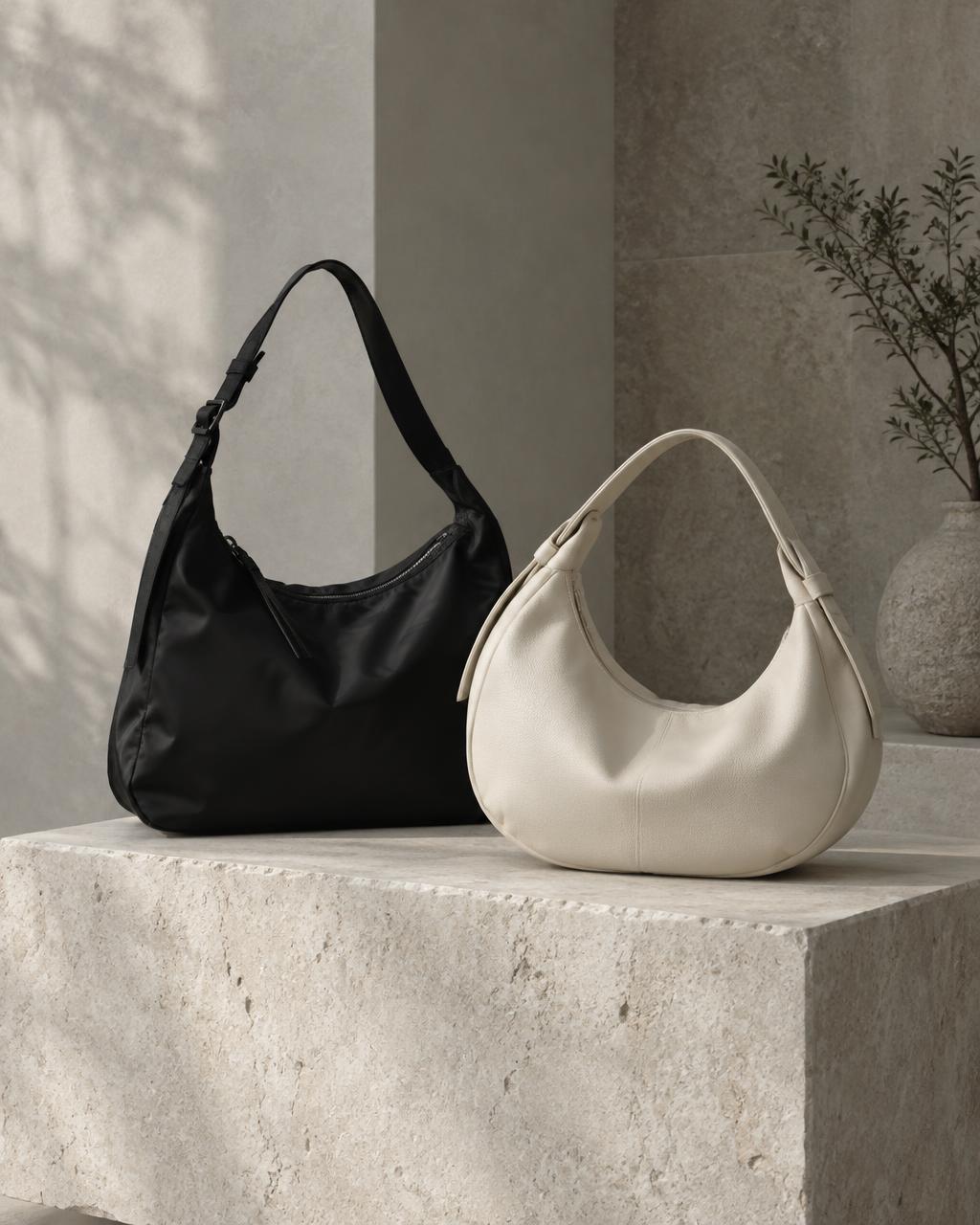 A nylon shoulder bag and a leather crescent bag on a stone plinth